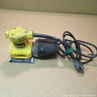 Full view of DeWalt palm sander with visible cord and dust collection bag, showing used condition and wear marks