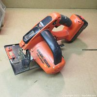 Black & Decker cordless circular saw on cardboard surface showing whole saw and battery pack.
