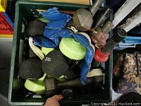 View of entire crate filled with various handheld weights including black neoprene dumbbells, green plastic dumbbell, metal dumbbells, and blue weighted gloves.
