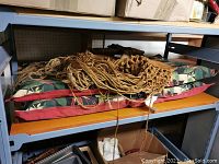 Two lounge chair cushions in tropical floral print, stacked on a shelf with a brown macrame hanging tapestry on top.