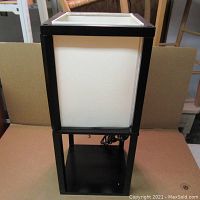 Full view of the modern style table lamp showing black wooden frame and white fabric shade on table.