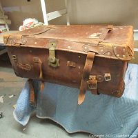 View of old leather trunk with brass lock, leather straps, rivets, and corner reinforcements showing wear and patina.