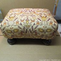 Full view of the ottoman showing the upholstery pattern and curved wooden feet.