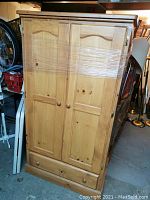Front view of the pine wardrobe showing two doors wrapped in plastic and bottom drawer.