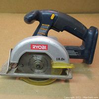Side view of Ryobi cordless circular saw showing the blade, handle, and base plate on a plain brown surface.