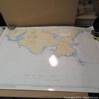 Photo showing the full nautical chart laid flat, with the coastlines illustrated in color, and parts of the edges held with paperweights.