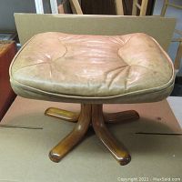 Front view of vintage leather ottoman showing padded top and wooden base with four legs.