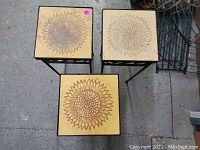 Top view of three small patio side tables with square tiled tops featuring sunflower patterns in beige and yellow colors.