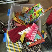 Plastic tub filled with assorted vintage and used fabrics in various colors and patterns such as stripes, plaids, floral, cartoon prints, and animal prints.