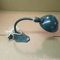 Green metal goose neck lamp showing full side profile with base, arm, shade, and attached white power cord.