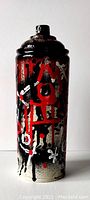 Front view of spray can sculpture showing red and black paint drips and abstract graffiti elements.