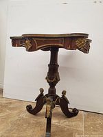 Full side view of the wooden side table showing the shape, pedestal and three legs with metal accents.