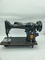 Black 1930's Singer sewing machine, side angle showing full body and mechanical details on platform and handwheel.