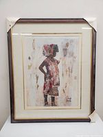 Frontal photo of the painting showing African child in traditional costume with mahogany frame, corners protected with white corner covers.