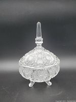 Crystal candy bowl with a lid and knob finial sitting on three rounded feet, showing clear crystal patterned design.