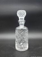 Crystal decanter standing upright showing cross cut pattern and stopper attached on top.