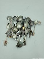 Top view showing a spread of approximately 25 assorted decorative souvenir spoons with various designs mainly from the UK