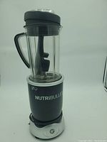NutriBullet blender base with attached tall plastic blending cup and lid in black and silver.