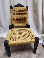 Front view showing woven jute seat and backrest with dark carved wooden frame and legs.