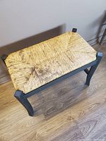 Top view of a black wooden bench with natural woven rush seat showing diagonal weave pattern.