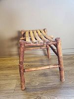 Side angle view of the primitive bamboo stool highlighting its slatted seat and tapered legs with cross supports.
