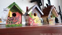 Set of three handcrafted decorative bird houses shown on a shelf. Each bird house is unique with floral and nature-inspired painting. All require cleaning.