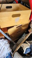 Wooden storage boxes stacked closely with other miscellaneous items including textiles and metal rods.