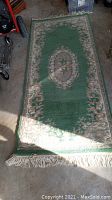 Full view of one green wool carpet runner with floral and ornamental patterns, fringed edges.