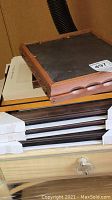 Wooden and white picture frames stacked on each other with some frames showing black backing and some glass fronts, some frames have scalloped wood edges.