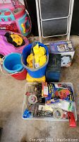 Overall view of the plastic buckets, gloves, boxed television lantern, small tools, and miscellaneous hardware items arranged on the floor.