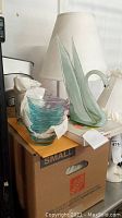 Photo of green glass swan statue, colored glass bowls, and items on cardboard box.