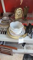Overview of multiple plates, ruffled milk glass bowl, decorative clock, and green glass vase