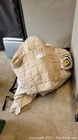 Beige quilt draped over a rolled rug with visible tags; placed on floor beside furniture.