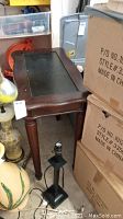 View of wood side table next to boxes and other items, showing leg style and overall shape.
