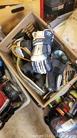 Box with hockey gloves, knee pads, and various other sports gear.