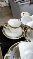 Close-up of cup and saucer showing green and gold decorative border, cup handle with gold trim.