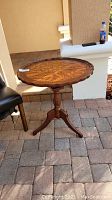 Full view of the round pie table showing the pedestal and three-legged base on a patio surface.