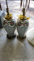 Pair of floral porcelain table lamps showing pink rose and stripe patterned bases with dark wooden bases, coiled yellow cords, and brass fittings.