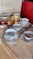 Front angled view of various vintage teacups with decorative saucers on a wooden surface