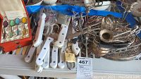 Wide view of multiple white handle knives, kitchen utensils, and metal casserole holder creating an overview of the lot contents.