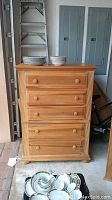 Full frontal view of the light wood dresser with 5 drawers and round knobs. Plates and bowls placed on top show scale and usage.