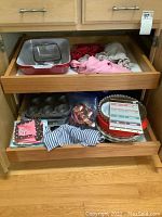 Full drawer view of kitchen items including bakeware, aprons, muffin tin, pie tins, and linens