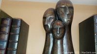 Close-up of bronze-tone art statue showing three stylized human heads with elongated necks in varying heights.