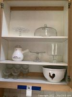 Shelved items showing glass cake stands, hot chocolate server, dessert bowls, and mixing bowls with rooster design