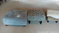 Three tufted upholstered ottomans of large, medium, and small sizes arranged side by side on carpet