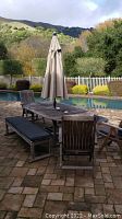 Full view of wood table set with umbrella in closed position beside pool