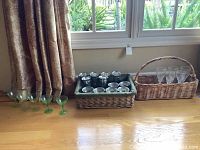 Wide shot of all glasses including 5 green-stemmed glasses, 8 pewter tall wine glasses and other glassware in wicker baskets.
