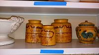 Shelf view of four ceramic jars with vintage text and decorative motifs