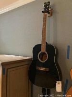 Rogue acoustic guitar hanging on wall showing full front profile and neck.