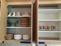 Cabinet shelf with stacked plates, bowls, and teacups including white and brown edged sets